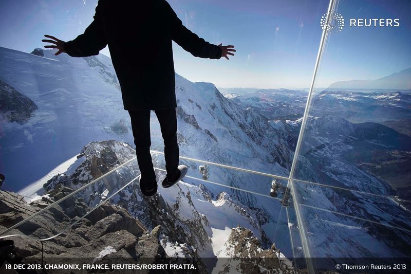 A journalist, wearing slippers to protect the glass floor, stands in the 'Step into the Void' installation during a press visit at the Aiguille du Midi mountain peak above Chamonix, in the French Alps